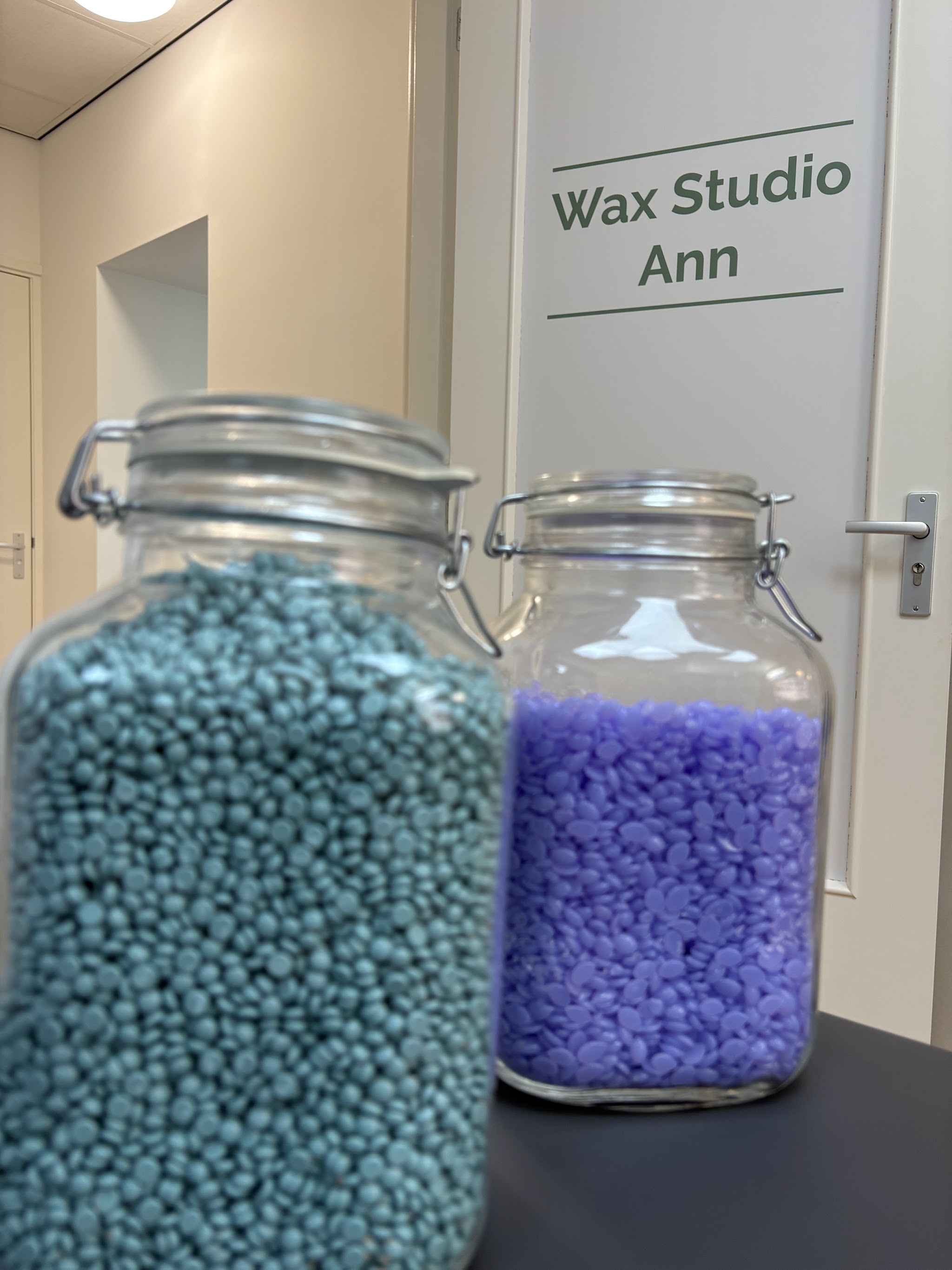 Twee glazen potten met waxparels, blauwgroen en paars, voor de deur met het logo